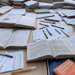 Mesa com livros de primeiros socorros e editais de concursos públicos, representando sobrecarga de candidatos no DF.