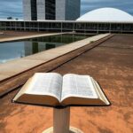 Bíblia aberta em sala legislativa de Brasília, representando reconhecimento como patrimônio e debate sobre laicidade.