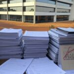 Edifício da Caesb em Brasília com documentos de concurso e relógio indicando prazos apertados, representando frustração de candidatos.