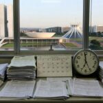 Mesa com pilhas de documentos burocráticos em escritório de Brasília, representando atrasos na Caesb e Adasa para inscrições no Conselho de Consumidores no DF.
