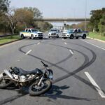 Cena de acidente na Epia em Brasília, com moto danificada e viaturas policiais, sem pessoas.