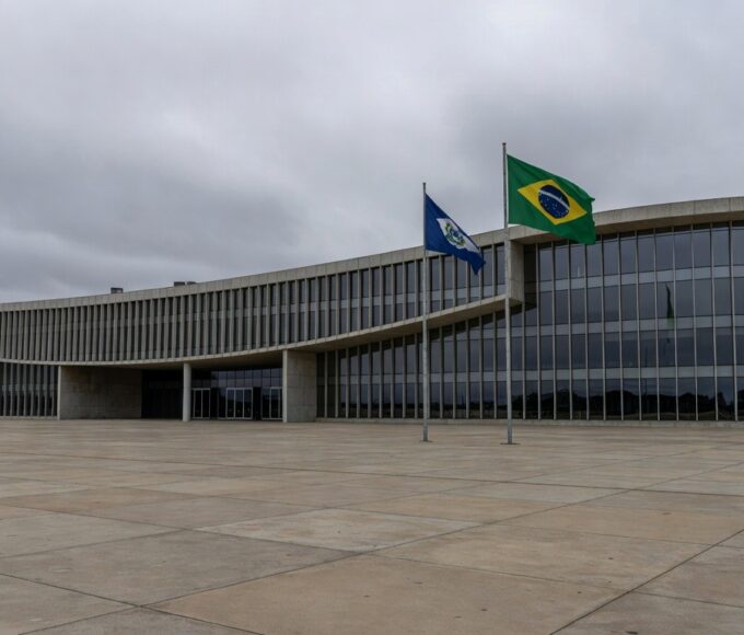 Fachada da CLDF em Brasília, contrastando com moradias precárias ao fundo, simbolizando ignorância a urgências sociais em sessão solene para corretores de seguros.