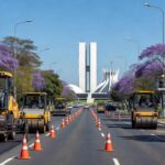 Manutenção urbana em avenida de Brasília, com equipamentos de pavimentação e sinalização no Distrito Federal.