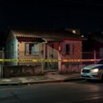 Cena de casa residencial em Samambaia Norte com fita de isolamento policial e viatura da PMDF, representando invasão e homicídio.